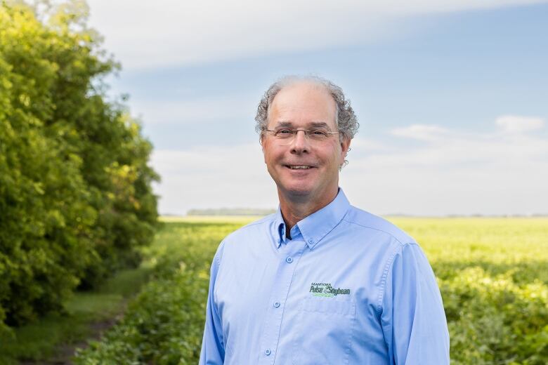 A man with glasses smiles in a field.