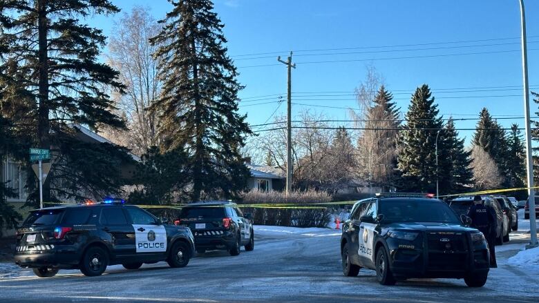 three police vehciles are parked on a street corner marked by police tape