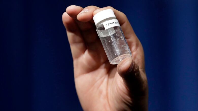 A hand holding a small clear glass tube with a white label.