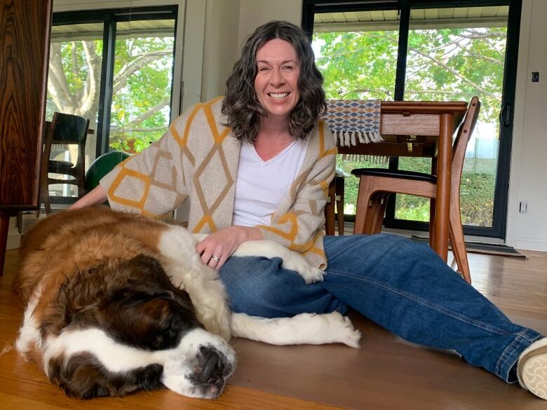 A smiling woman sits on the floor with a large St. Bernard.