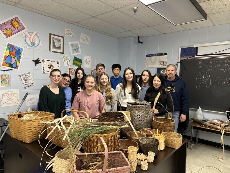 Several teenagers and a man stand together in a classroom for a group photo. In front of them is a table covered in baskets.