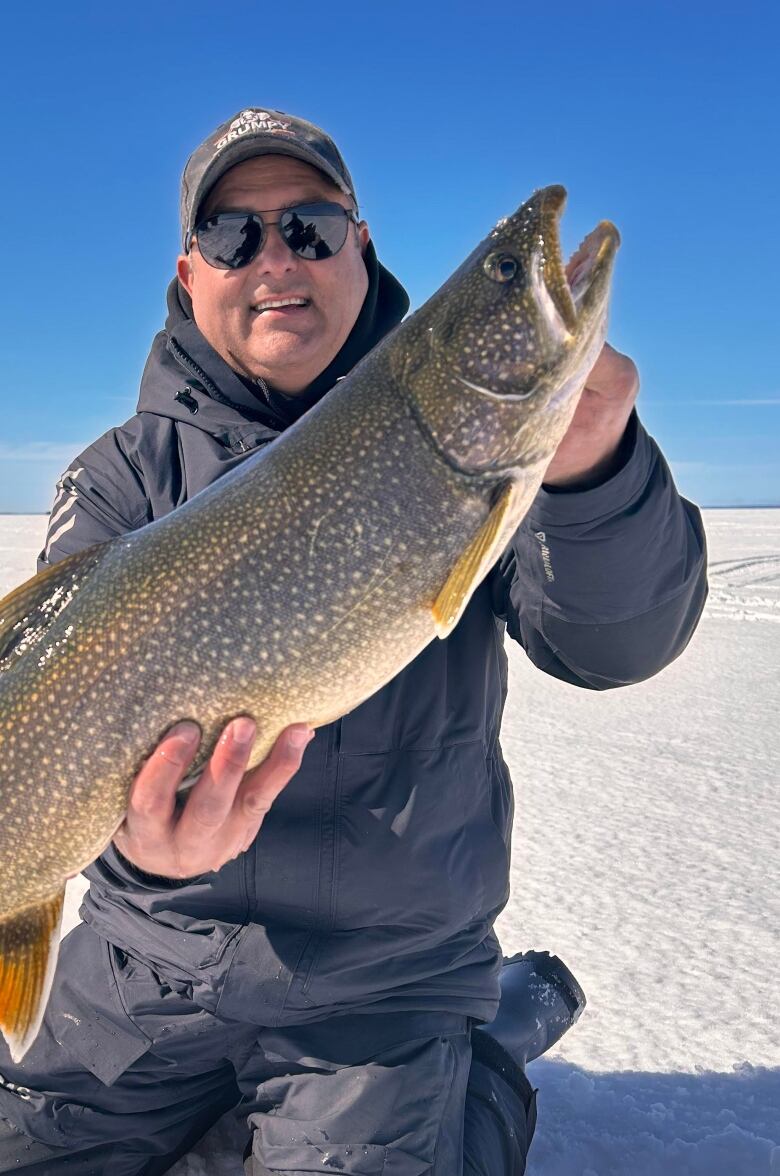 photo of a man holding a fish on an icy lake