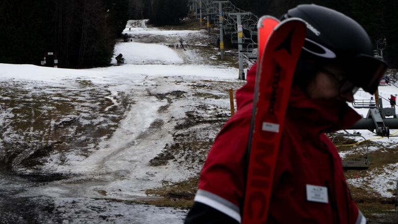 A snowboarder is pictured in profile as they cross a mushy, somewhat snowy slope. A chairlift is visible behind them.