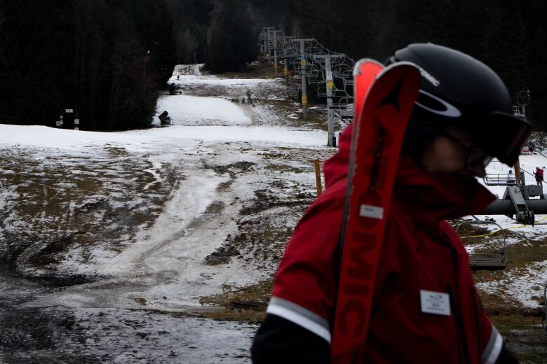 A snowboarder is pictured in profile as they cross a mushy, somewhat snowy slope. A chairlift is visible behind them.