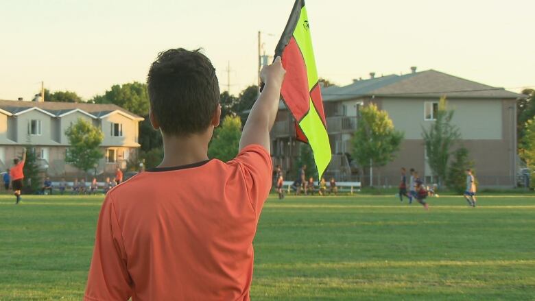 A soccer referee raises a flag. They are standing with their back to the camera. 