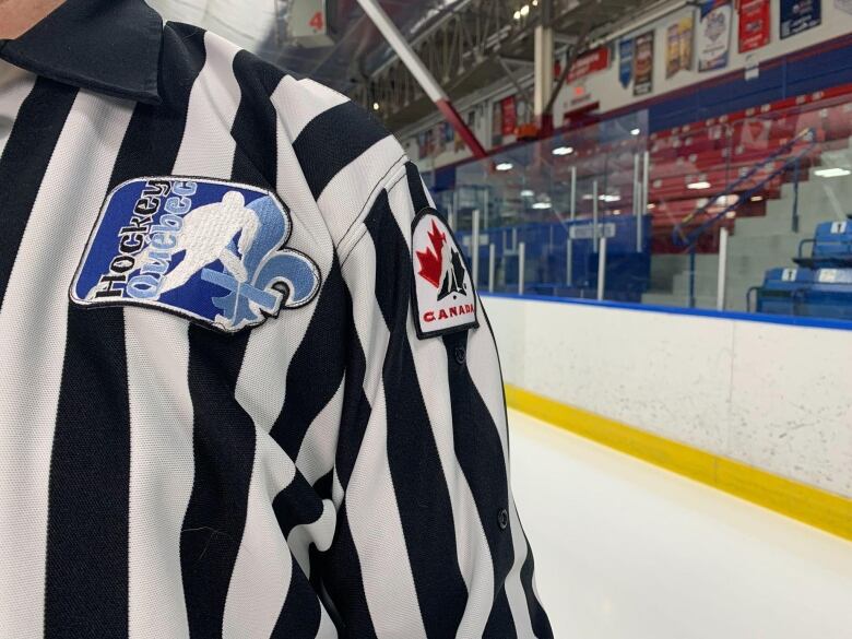 The shoulder of a referee in a hockey arena. His badge says Hockey Quebec and Hockey Canada 