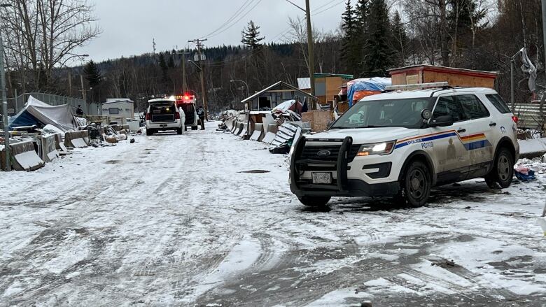 An RCMP vehicle on a snow covered road, with flashing red lights from an ambulance in the background. 