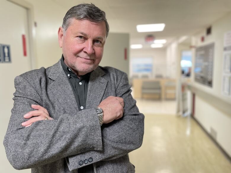 A man in a grey jacket stands in a hospital hallway.