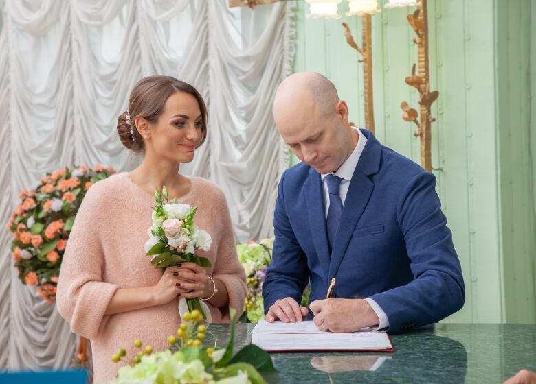 A man and woman stand together signing marriage papers