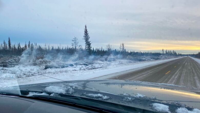 Smoke rises from snow along a road.