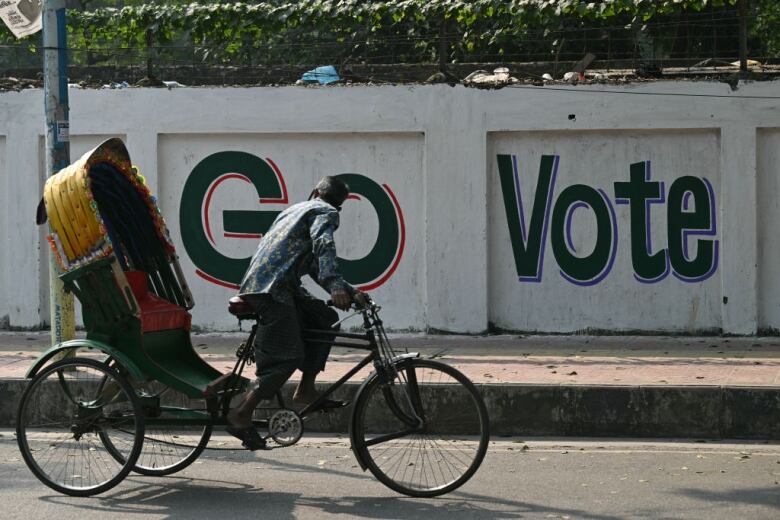 A rickshaw passes in front of a mural on a wall urging people to vote in Dhaka, Bangladesh.