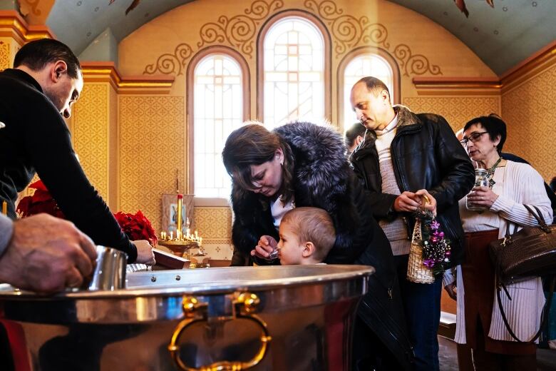 A woman helps a child drink blessed water during a church service.