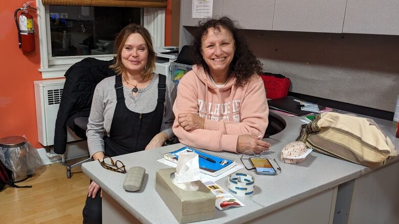 Two women sit and smile behind a desk 