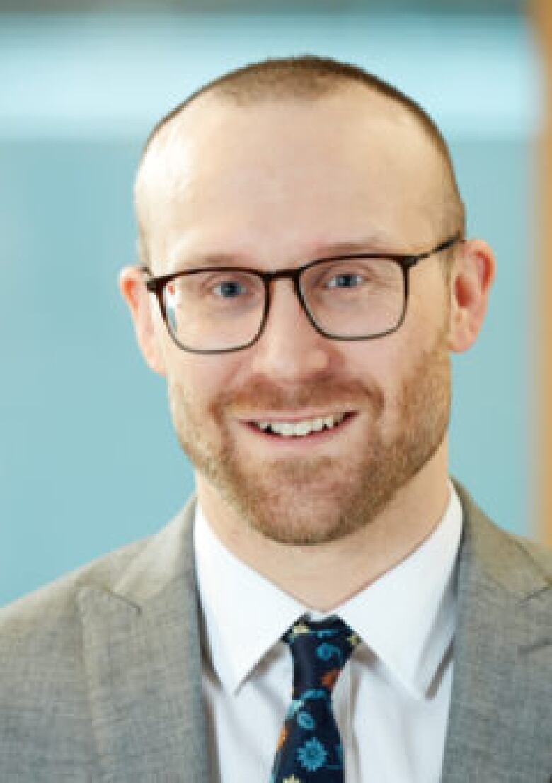 A balding man wearing a grey suit and glasses