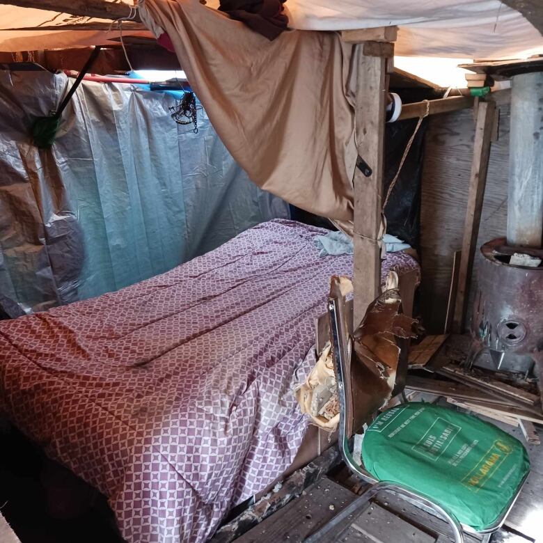 A bed with a bedspread and a broken chair in a wooden shack.