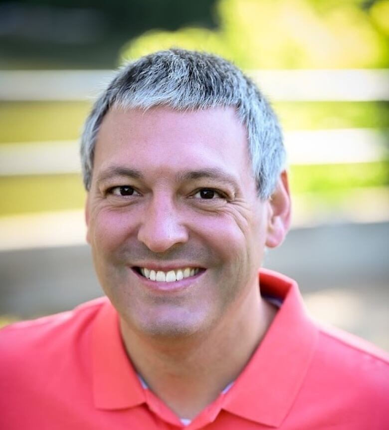 A man in a salmon-coloured shirt poses for a photo. 