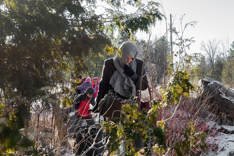 A woman with children following behind her in the woods.