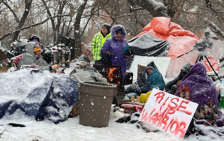 A group of people sit around a cluster of snowy tents and tarps. 