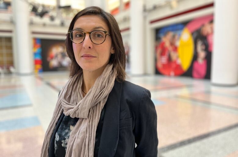 A woman in a scarf and glasses looks to camera in the CBC Toronto atrium.