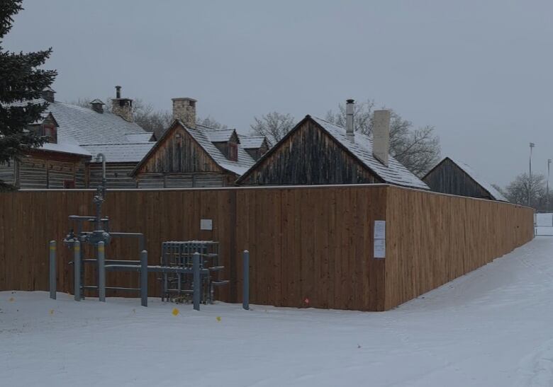 A brown fence stands around a fort surrounded by snow.