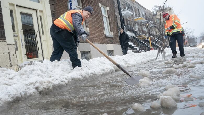 Workers attempt to unclog a storm drain filled with icy water. 