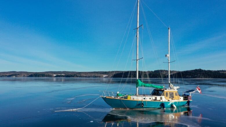 A double-masted sailboat is frozen into the ice on a body of water. 