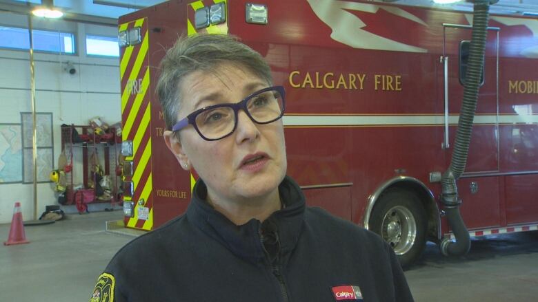 a woman with glasses stands in front of a fire truck