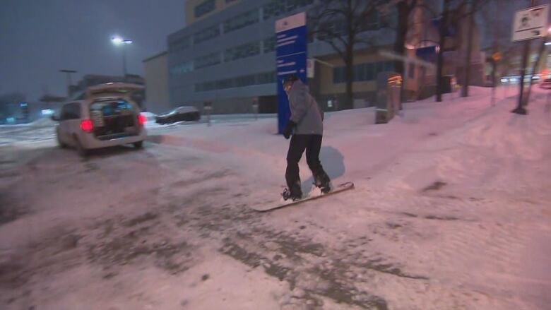 A person snowboards on a sidewalk in Quebec City early in the morning while it is still dark. 