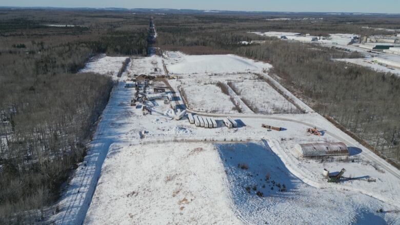 A large snowy site with a winding road and several piles of material and trucks. 