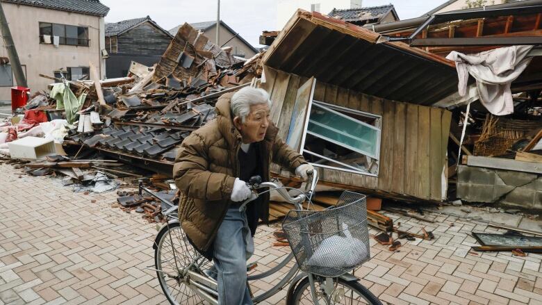 A man on bicycle moves past collapsed houses in Wajima, Ishikawa prefecture, Japan Thursday, Jan. 11, 2024. A powerful earthquake slammed the western coastline of Japan on New Years Day. (Kyodo News via AP)