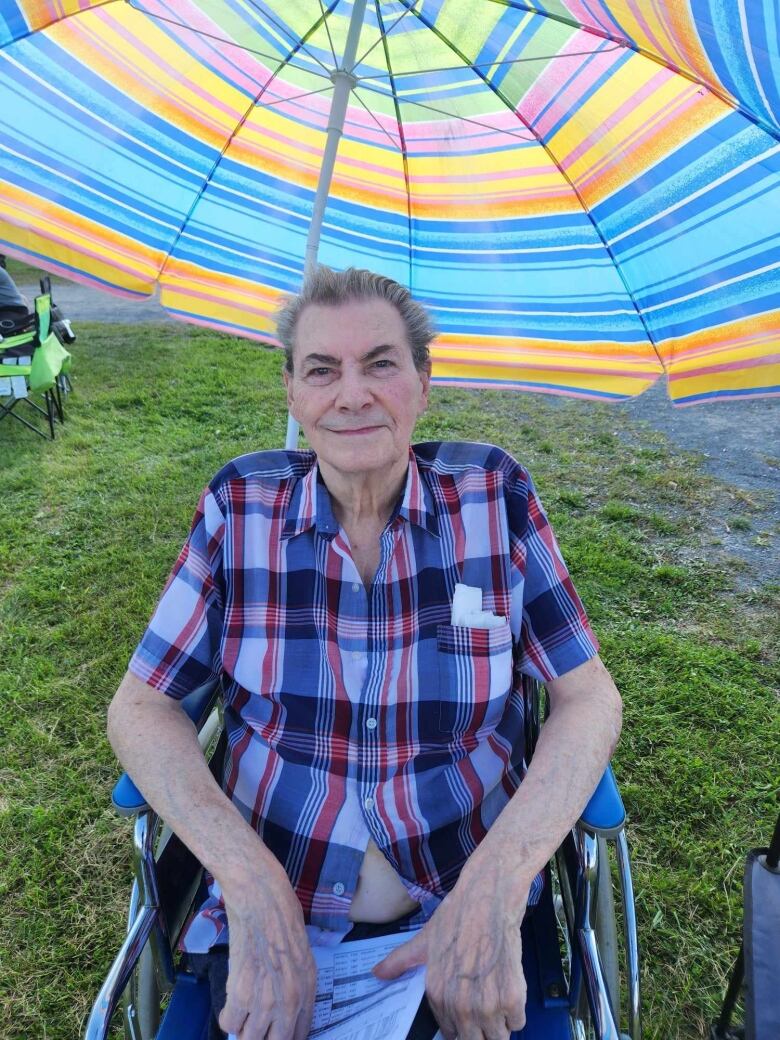 A man sitting in a chair with a colourful umbrella over him. 