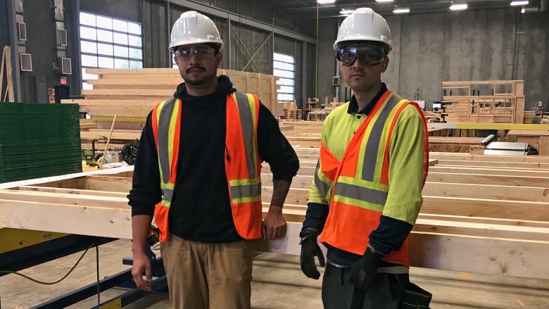 Two men dressed in construction gear are seen standing at the site of a construction workshop.