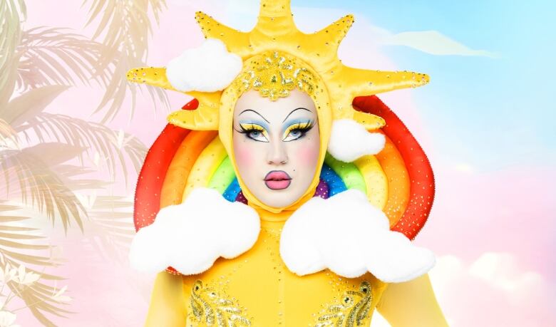 A drag queen strikes a pose while wearing a colourful costume featuring the sun, a rainbow and clouds.