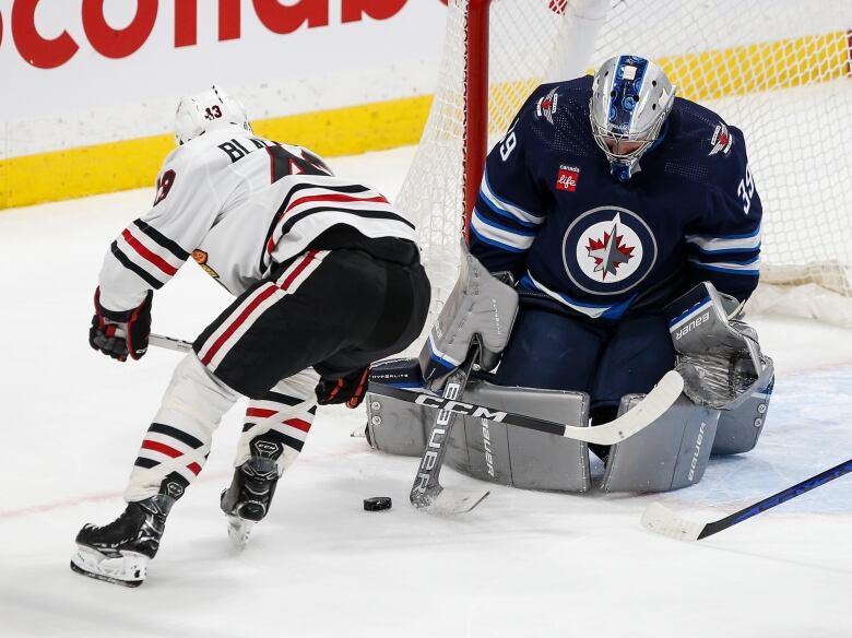 A goaltender in blue makes a save with his right pad while a Chicago Blackhawks player skates past.