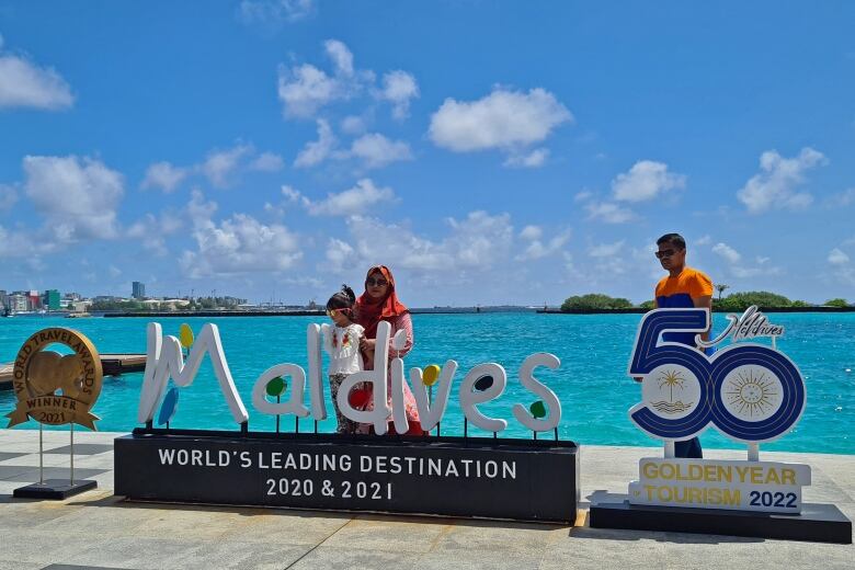 Tourists stand and pose for photos at the Mal international airport beside a sign promoting the Maldives as a top holiday destination. 