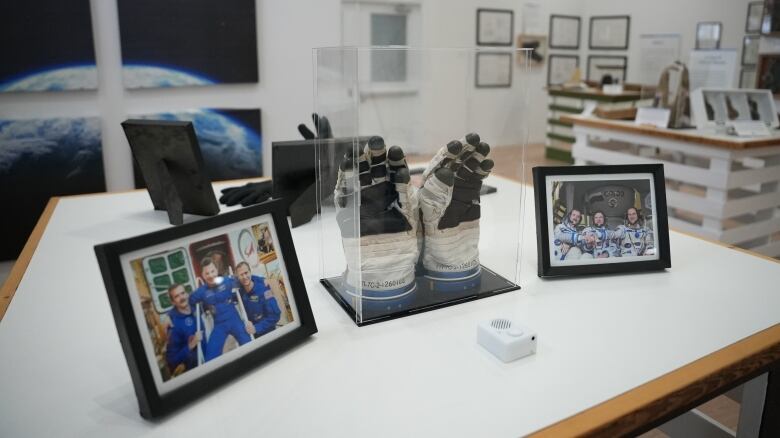 Gloves inside of a glass box, next to it are pictures of astronauts 