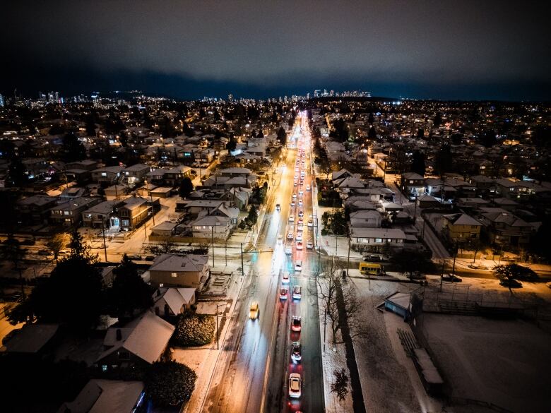 An aerial image of rows of cars stuck on a road flanked by snowy houses.