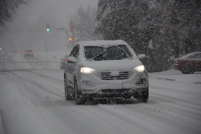 An SUV covered in snow driving on a snowy road.