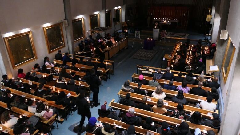 Overhead shot of people holding candles while sitting in pews in a dimly lit chapel.