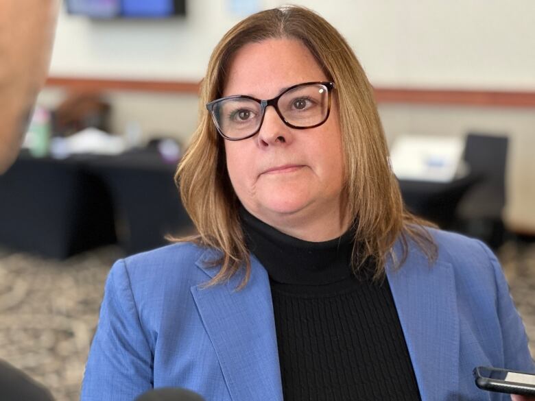 A woman in a blue blazer and black sweater looks upward.