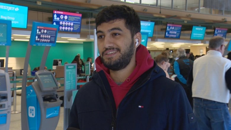 Man in a red hoodie and black jacket in front of airport check in.