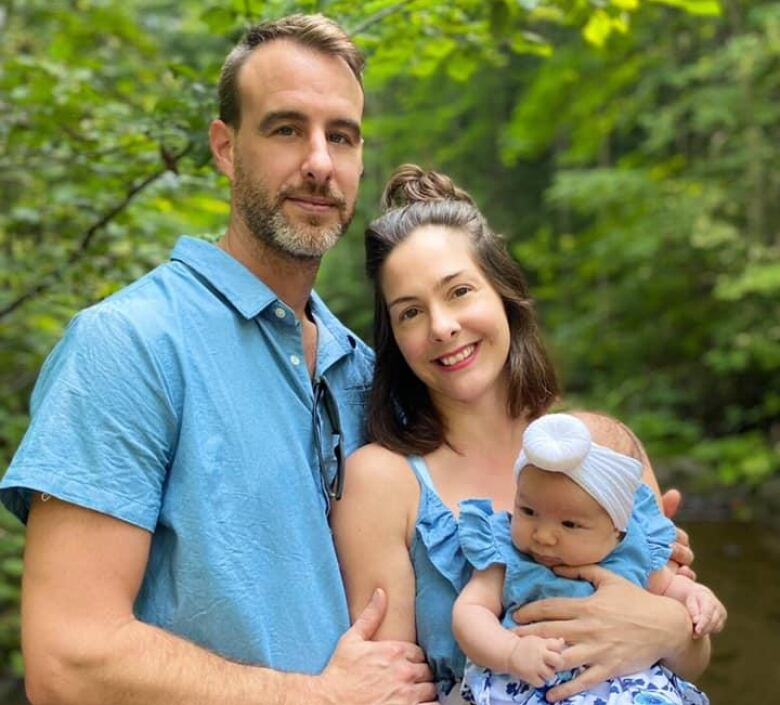 A couple smiles at the camers while holding a baby 