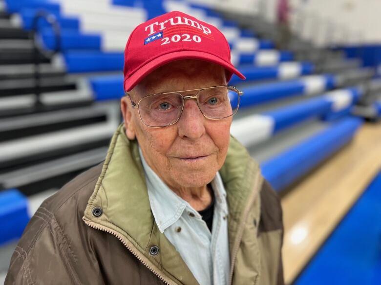 Elderly man in glasses and red cap that says Trump 2020