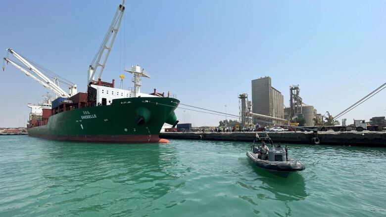 A cargo ship in port with a rubber inflatable boat near it.