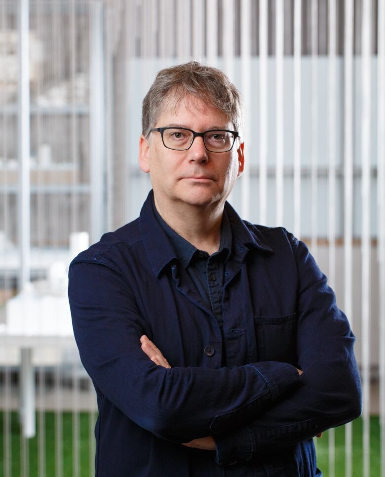 A man in glasses with arms folded, wearing dark clothes.