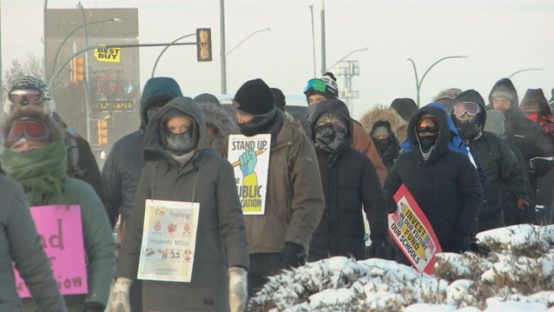 A line of people in cold-weather clothing walk a picket line with signs.