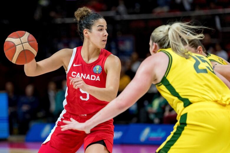 A women's basketball player possesses the ball with her right hand while being guarded.