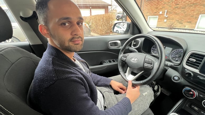 Man sits behind steering wheel peers back at the camera.