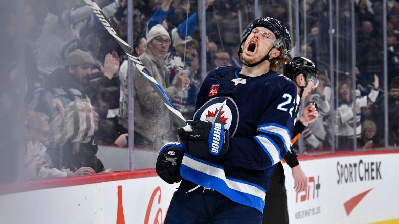 A Winnipeg Jets player in navy blue closes his eyes and shouts in celebration.