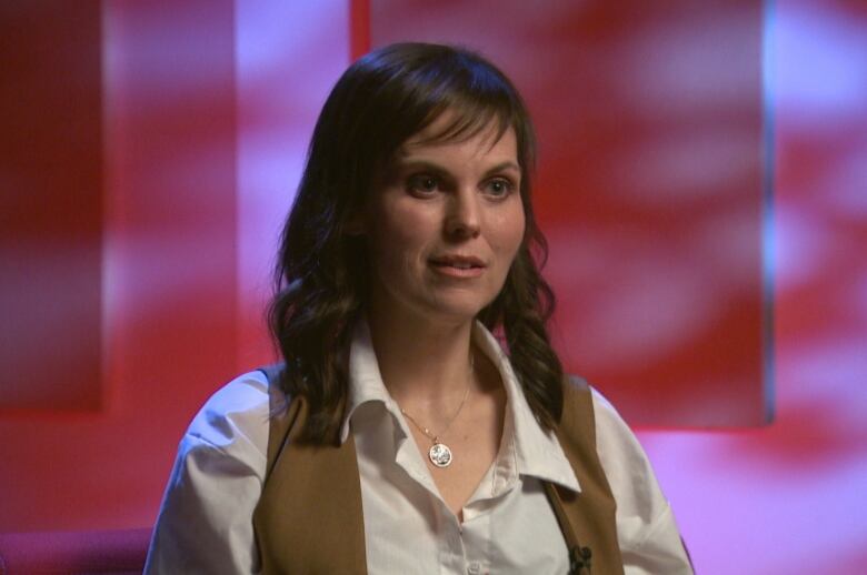 A woman wearing a white shirt sits in a chair in a dimly lit room. 